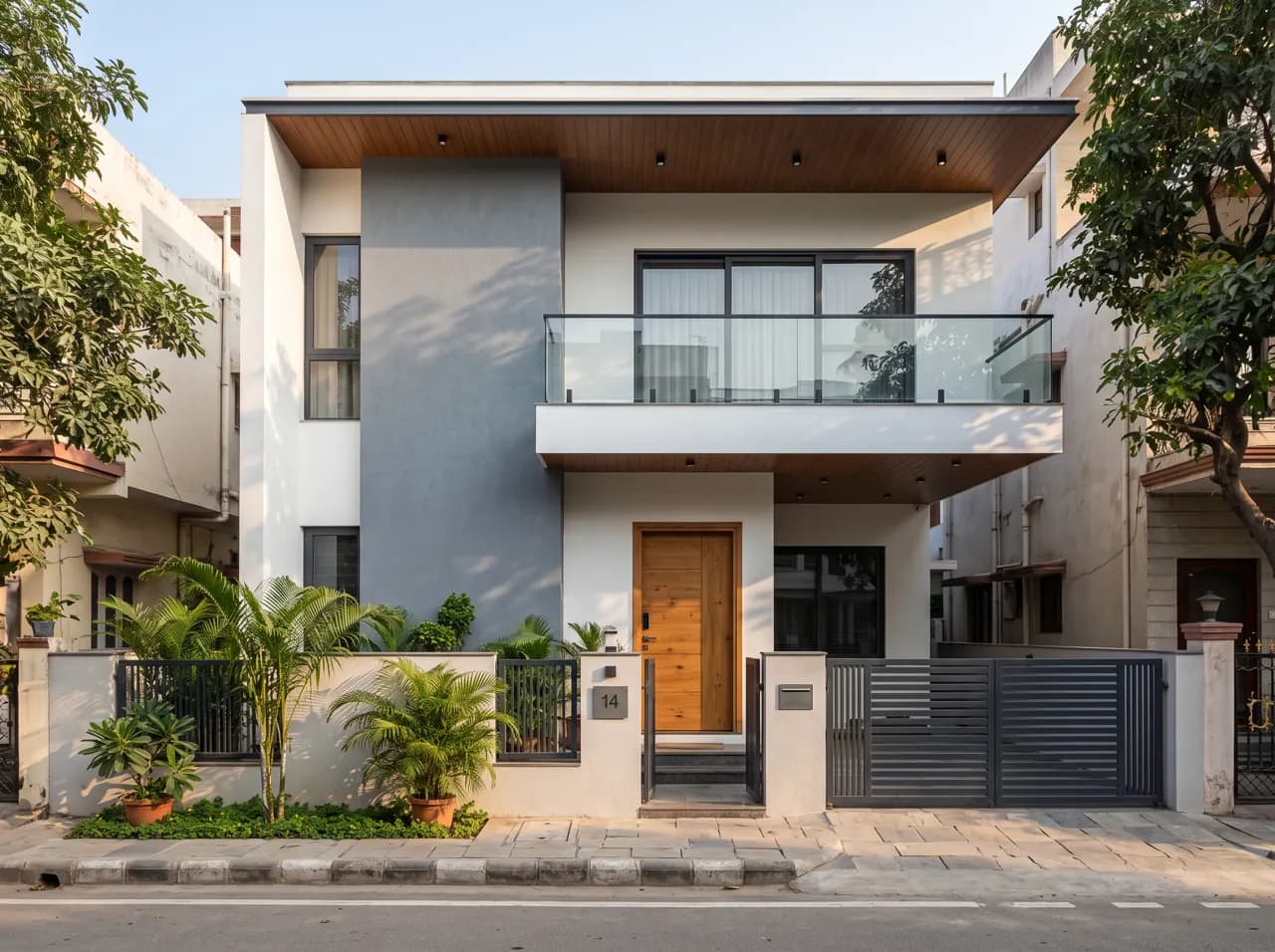 Modern Indian house front design with grey textured panel, glass balcony and wooden main door