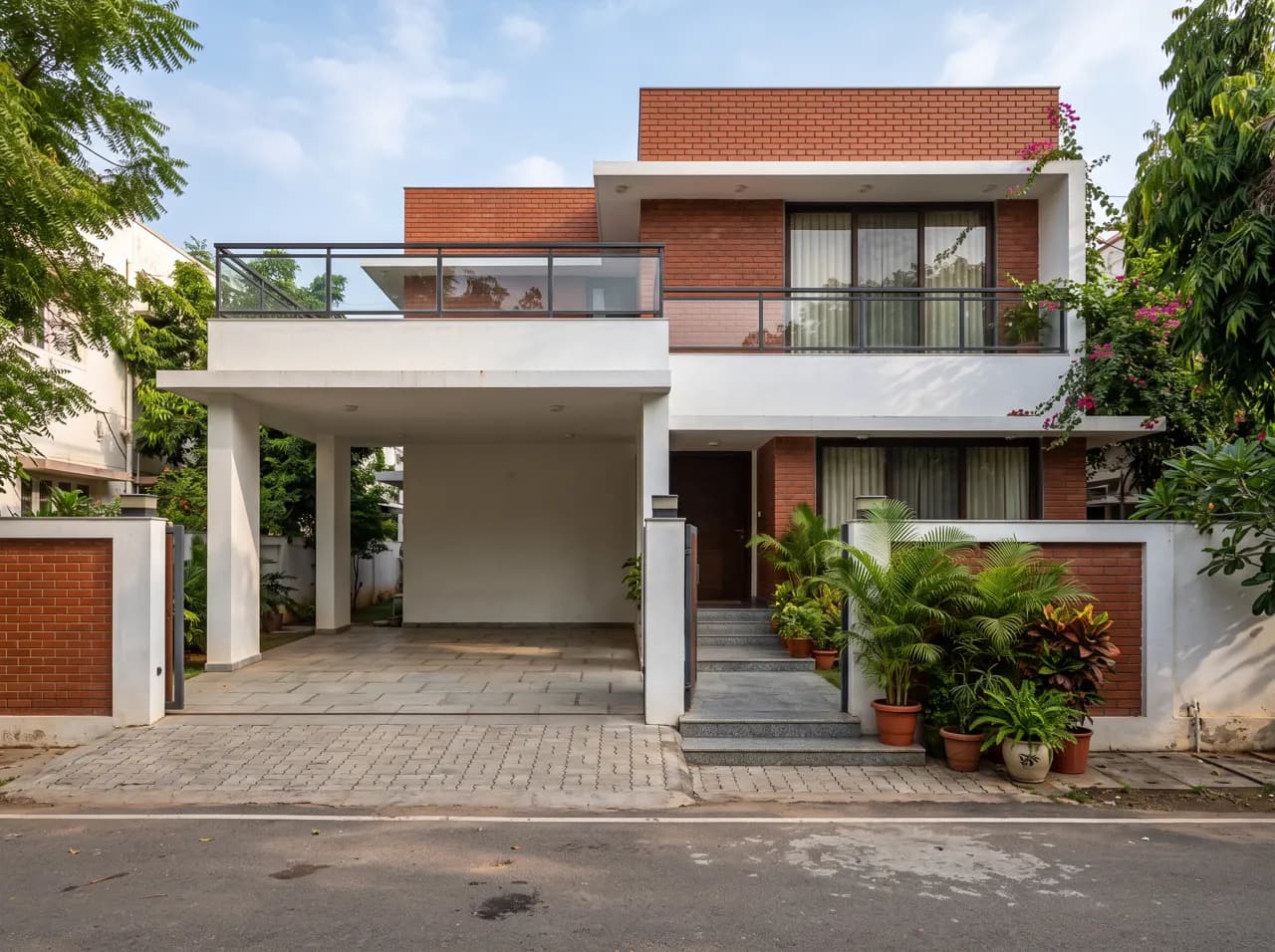 Indian home front with exposed brick volumes, portico and glass balcony railing
