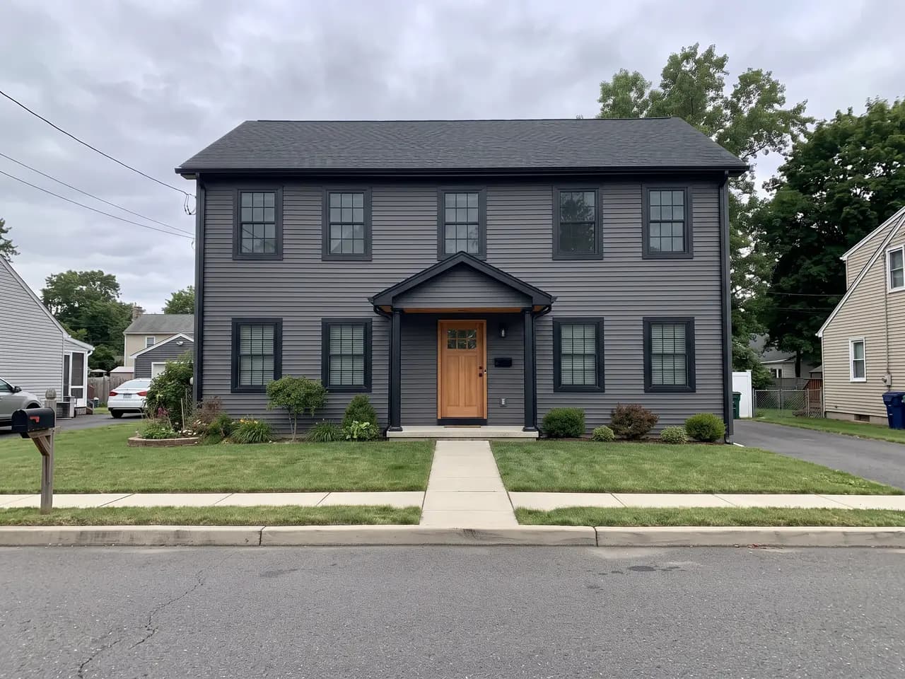 House exterior repainted in a charcoal and cedar colour scheme: charcoal grey walls, black trim and a cedar front door — after