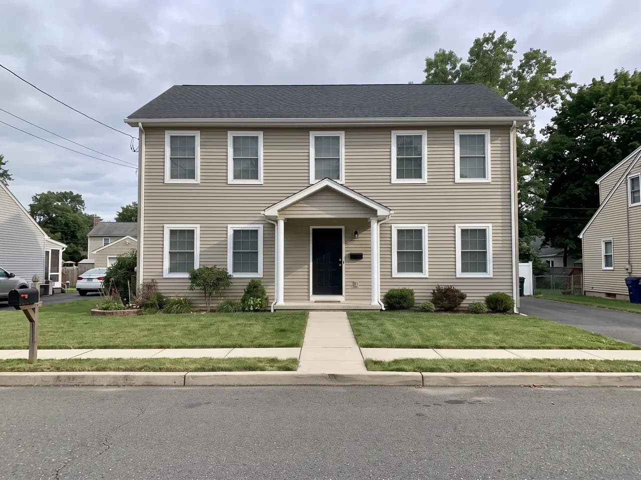 House exterior repainted in a classic greige colour scheme: greige walls, bright white trim and a black front door — after