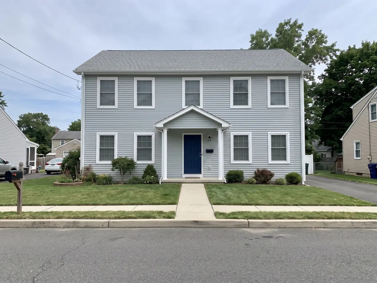 House exterior repainted in a coastal blue-grey colour scheme: pale blue-grey walls, bright white trim and a navy front door — after