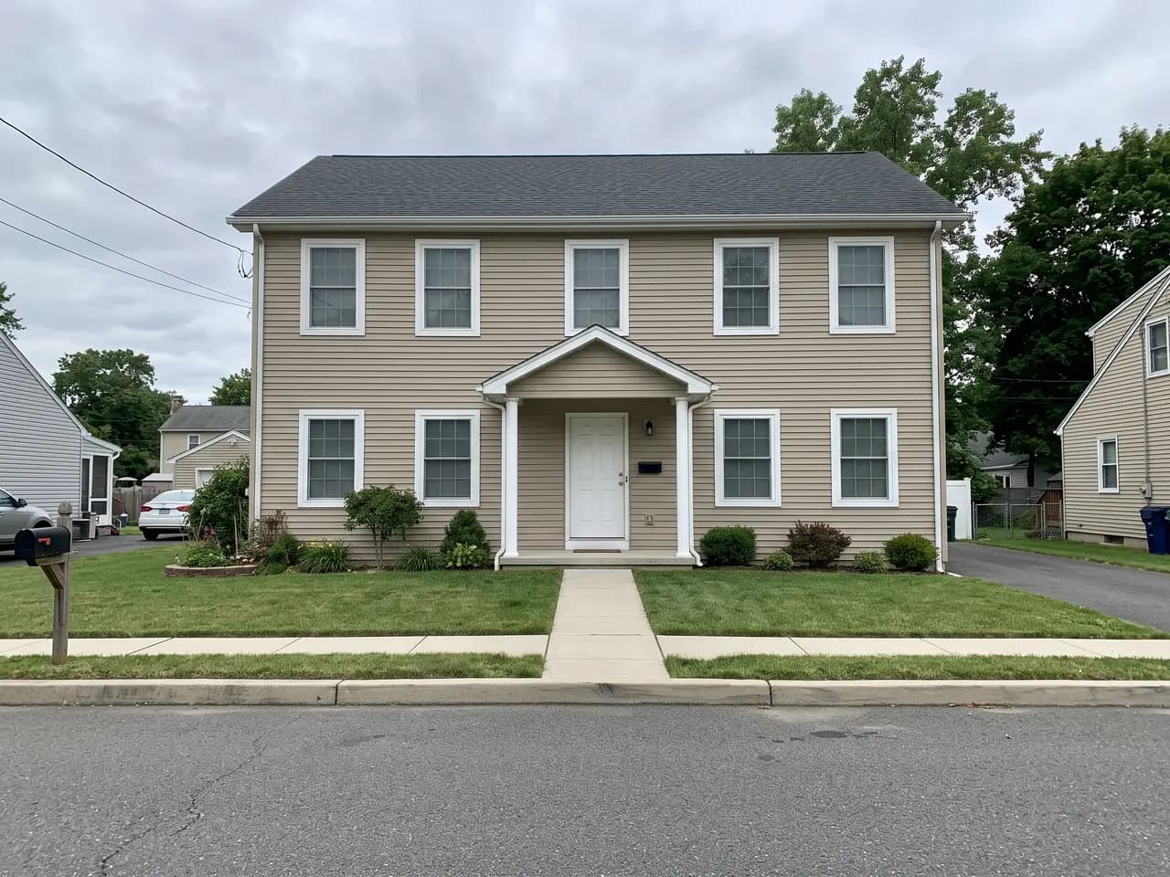 House exterior repainted in a modern farmhouse colour scheme: warm white walls, black trim and a natural oak front door — before