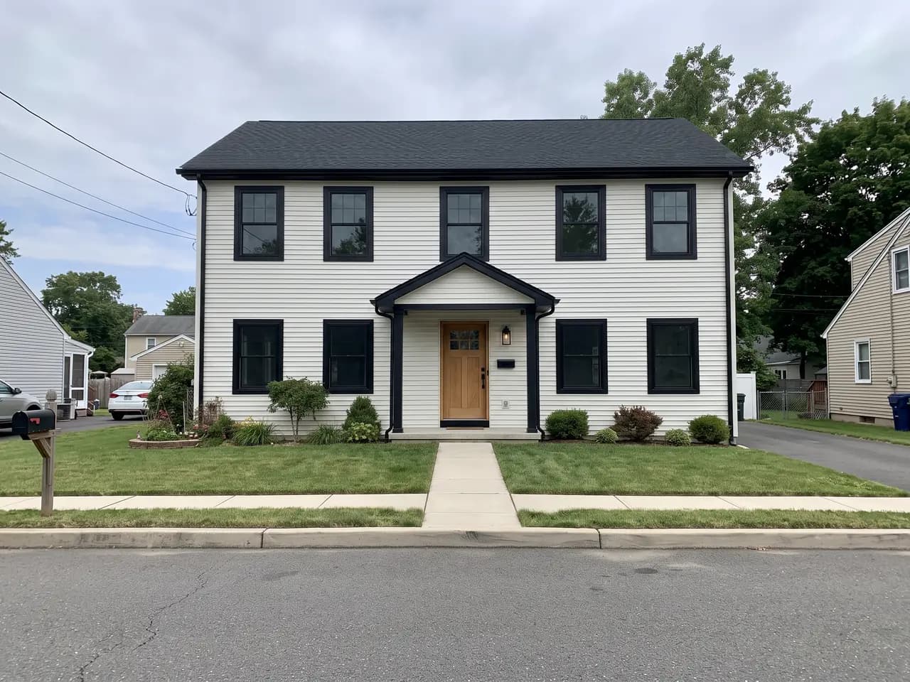 House exterior repainted in a modern farmhouse colour scheme: warm white walls, black trim and a natural oak front door — after