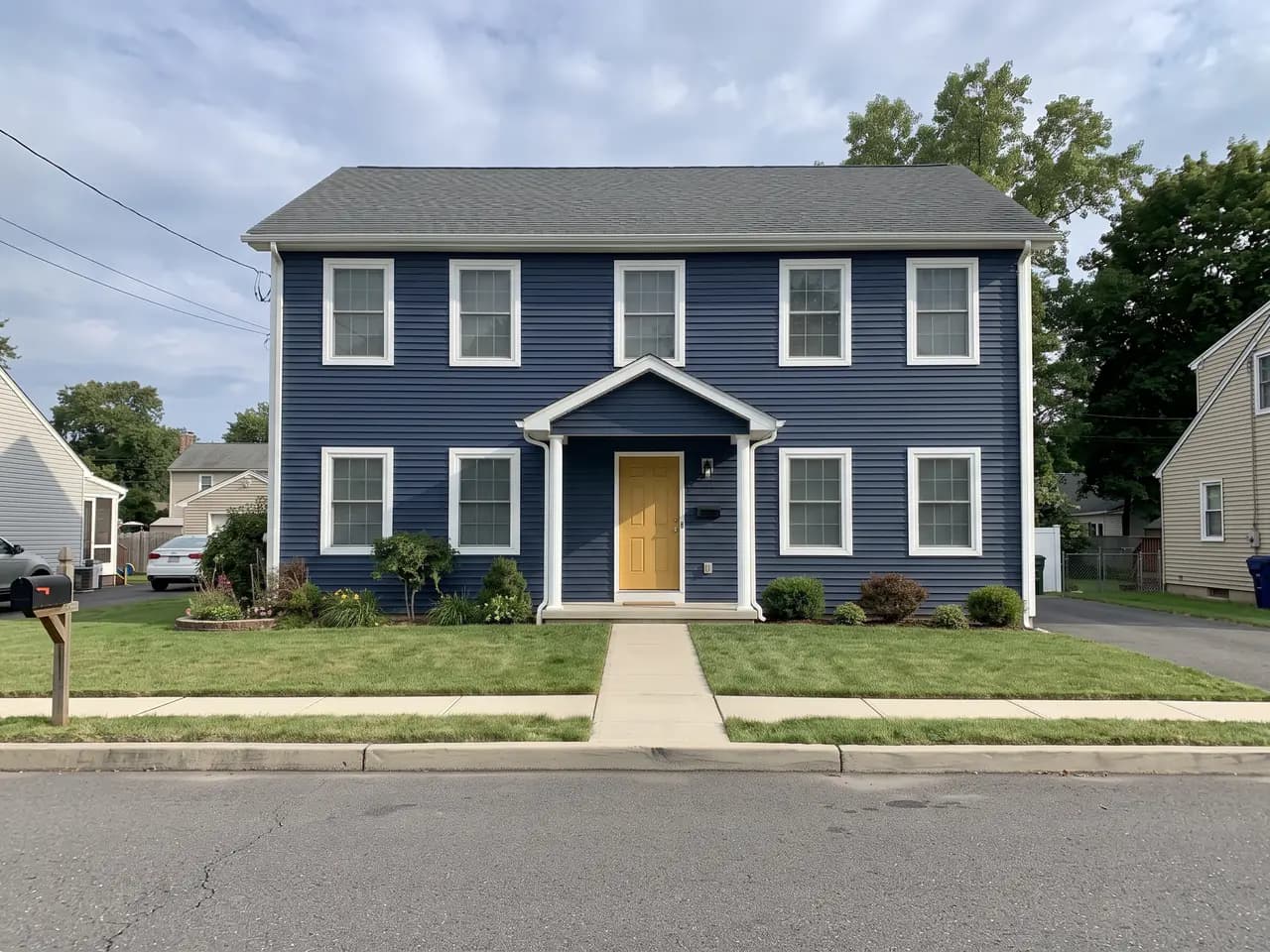 House exterior repainted in a navy and white colour scheme: navy blue walls, bright white trim and a mustard yellow front door — after