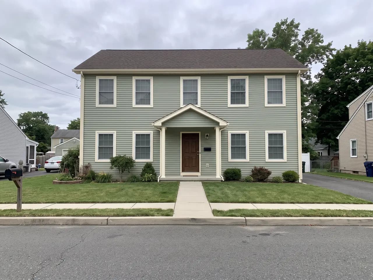 House exterior repainted in a sage and cream colour scheme: sage green walls, cream trim and a walnut brown front door — after